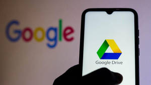 手拿著手機顯示Google Drive應用程式，背景有模糊的Google標誌。