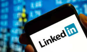 手拿著手機顯示LinkedIn應用程式，背後有股票市場數據。
