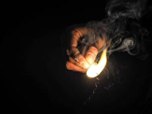一隻手拿著點燃的火柴，在黑暗背景上投射出溫暖的光和煙霧。