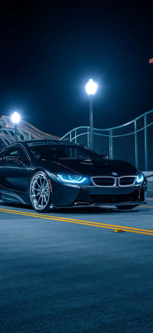 黑色BMW i8跑車在夜間明亮的燈光下停放在賽車場上。 — Pixel 8a 壁紙