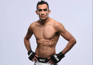 一位赤裸上身的男性MMA拳手戴著UFC手套在攝影棚中擺姿勢。
