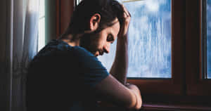 男人在雨窗旁低頭，手放在頭上