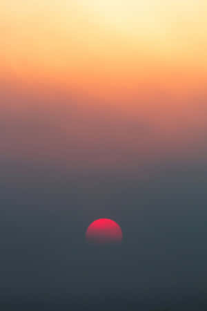 紅色太陽在薄霧後落下，天空呈現橙色和紫色