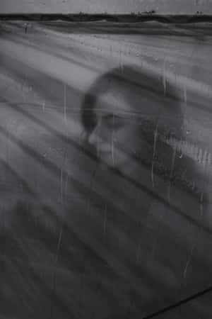 透過雨水濕潤的玻璃看到的女人臉龐，伴隨著柔和的光線。