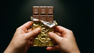 在深色背景前，手從金箔中打開朱古力棒。 — 朱古力 壁紙