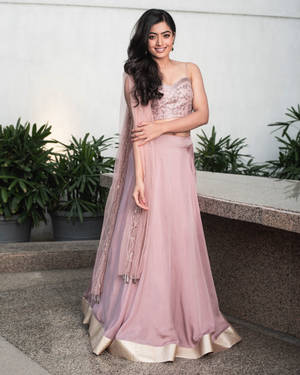身穿粉紅色 lehenga 的女性在戶外石台和盆栽旁微笑。 — 粉紅動漫美學 壁紙