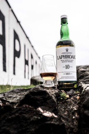 Laphroaig 10年威士忌酒瓶和品酒杯放在岩石上，靠近有品牌標誌的牆壁。