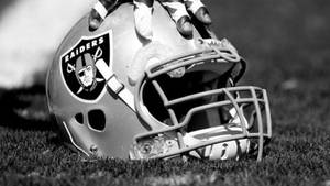 Raiders 美式足球頭盔放在草地上，戴手套的手握住它。