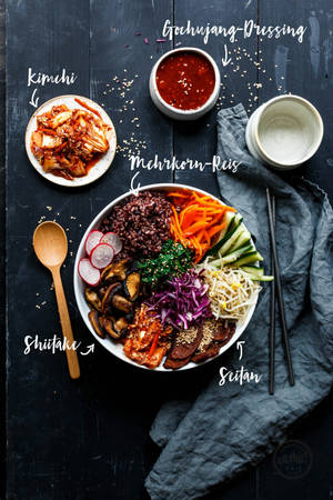 一碗色彩繽紛的韓國石鍋拌飯，配有黑米和配料，放在深色木桌上，附有筷子。 — 清新 GIF 壁紙