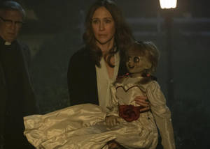 女子在夜晚拿著一個令人毛骨悚然的娃娃，附近有牧師。