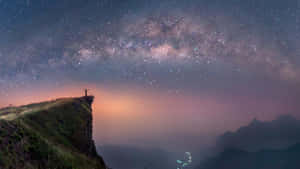 人站在懸崖邊，在星空下高舉雙臂