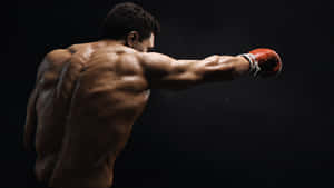 一個肌肉發達的拳擊手在黑暗的攝影棚中揮拳，背上汗水閃爍。 — 拳擊 壁紙