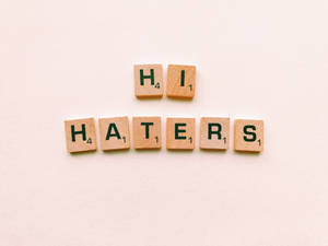 木製 Scrabble 字母牌在米色背景上拼出「Hi Haters」。