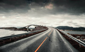 彎曲的海岸道路在風暴天空下通往橋樑，背景有山脈。