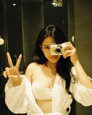 身穿白色長袍的女士拿著相機在鏡子自拍中做出和平手勢。