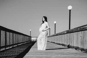 穿著蕾絲裙的孕婦站在有街燈的木製碼頭上