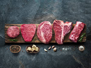 五塊生牛肉扒配調味料放在木板上，以深色石面為背景。