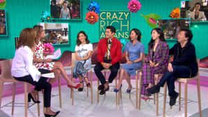 六個人在「Crazy Rich Asians」的彩色電視錄影廠佈景中坐在凳子上大笑。