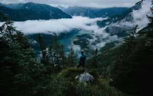 人站在懸崖邊緣，俯瞰被常綠樹木環繞的迷霧山湖。