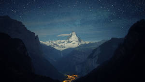 星空下白雪覆蓋的山峰，下方發光的村莊