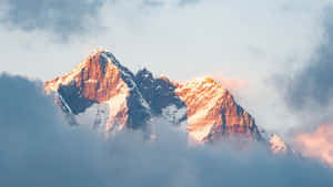 日出時從雲層中浮現的積雪山峰