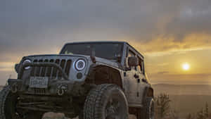 泥濘的Jeep Wrangler在日落時分停在山丘上，背景是金色的天空和遠山。