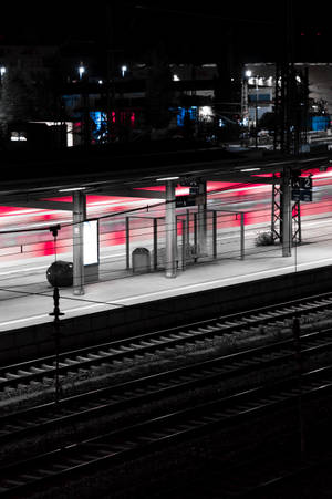 夜間火車站，黑暗鐵軌上有移動火車的紅色光跡。