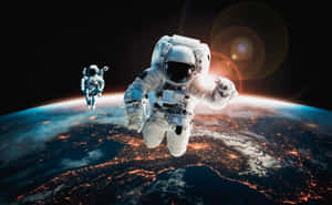 兩名太空人在夜間的地球上空漂浮，城市燈光可見。 — 太空 壁紙