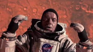 穿著NASA太空衣的太空人站在紅色行星表面，背後有隕石坑地形。