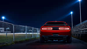 紅色Dodge Challenger在夜間停泊在體育場燈光下，靠近圍欄和看台。