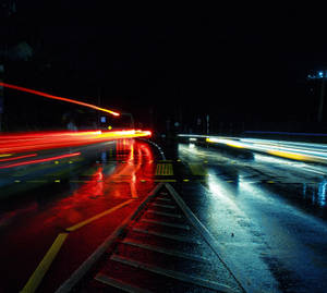 夜間道路，濕漉漉的路面上有紅色和白色的車燈條紋。
