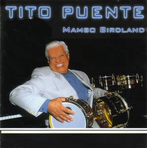 Tito Puente 在藍色霓虹文字的舞台上微笑著拿著鼓。