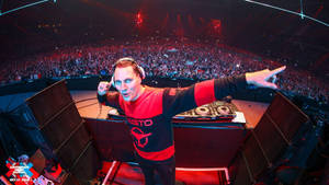 DJ Tiësto 在一個擠滿人的音樂會場地表演，現場有發光的紅色燈光。