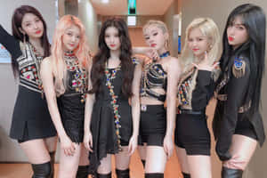 六位女性K-pop偶像穿著黑色閃亮服裝在室內擺姿勢。