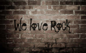 磚牆上的塗鴉寫著 We love Rock，帶有骷髏眼睛和閃電。