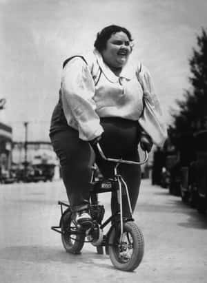 一個女人笑著騎著小型單車，行駛在停有汽車的街道上。