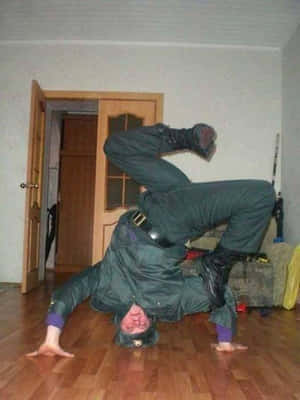 身穿綠色制服的人士在室內木地板上做倒立。