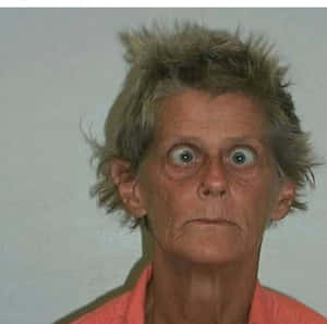一位頭髮灰白蓬亂、雙眼圓睜的老婦人直視鏡頭。