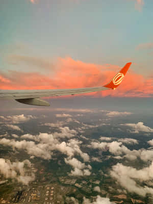 飛機翼在日落時分飛越雲層，伴隨色彩繽紛的天空與下方大地。