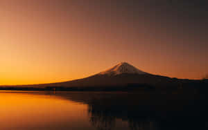 富士山在日落時分倒映在平靜的湖面上，周圍有深色的蘆葦。