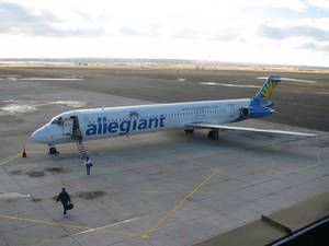 Allegiant Air 飛機停在停機坪，人們正在登機並攜帶行李行走。