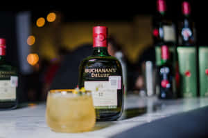 夜晚大理石吧檯上的 Buchanan's Deluxe 威士忌瓶和雞尾酒，帶散景燈光。
