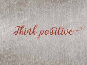 紅色閃粉草書文字寫在帶紋理的銀色牆上，內容為「Think positive」