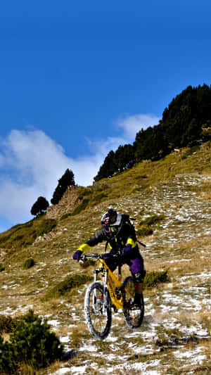山地自行車手騎著亮黃色自行車從積雪的草坡上滑下。