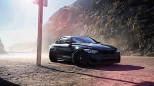 日落時分，黑色BMW M4雙門跑車停泊在懸崖旁的塵土路上。 — 16:9 壁紙