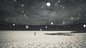 一個人在夜晚獨自走在結冰的湖面上，雪花飄落。 — 傷心 壁紙