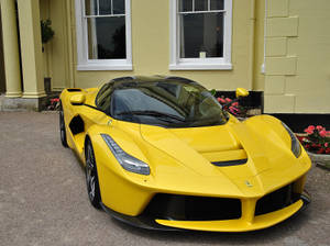 黃色法拉利 LaFerrari 停在一間黃色房子前，旁邊有花。