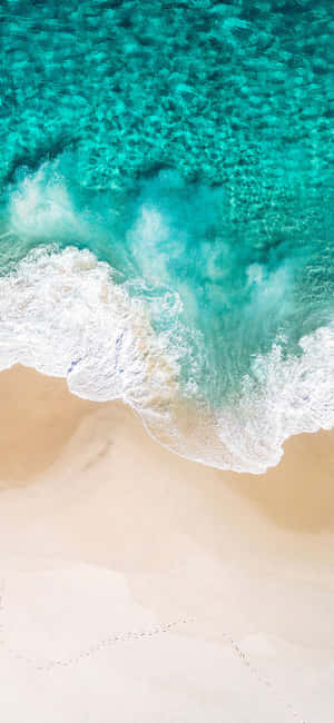 從空中俯瞰，碧綠色的海浪沖刷著帶有腳印的沙灘。 — Huawei nova 15 Max 壁紙