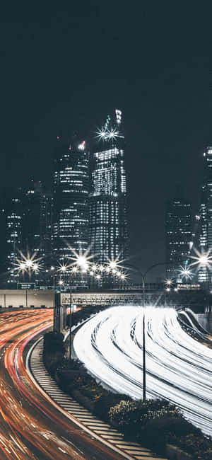 夜間城市景觀，在發光的摩天大樓下彎曲的高速公路上有汽車燈光條紋。