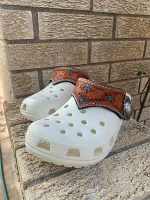 白色Crocs鞋，帶有裝飾性皮革帶，放在磚牆附近的石階上。